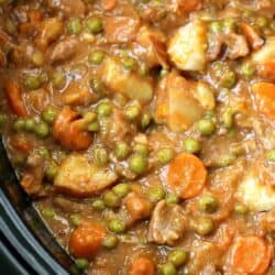 A close-up of a hearty beef stew containing carrots, peas, and chunks of potatoes.