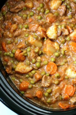 A close-up of a hearty beef stew containing carrots, peas, and chunks of potatoes.