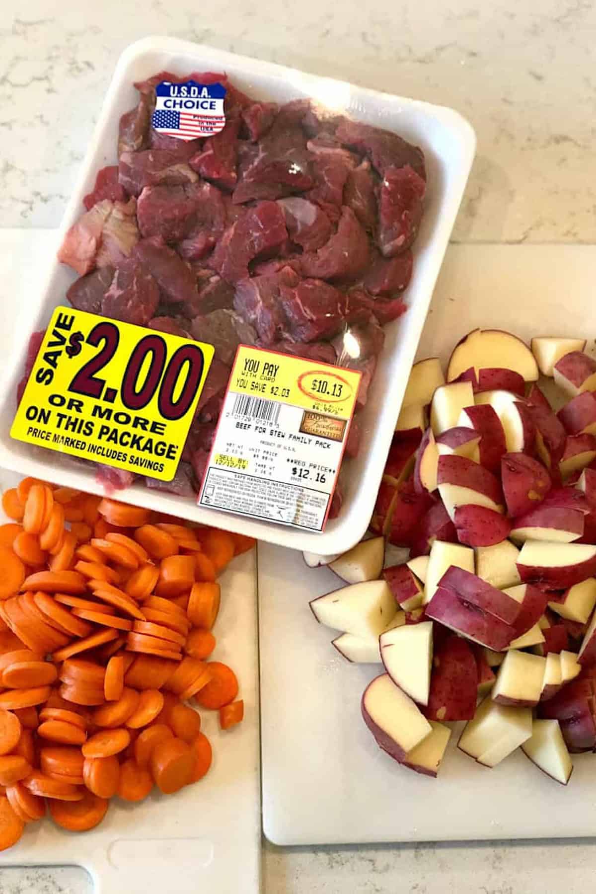 Image of a package of U.S.D.A. Choice beef stew meat priced at $10.13, a cutting board with sliced carrots, and another cutting board with chopped red potatoes.