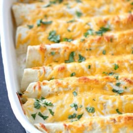 A baking dish filled with cheese-topped enchiladas garnished with chopped cilantro.