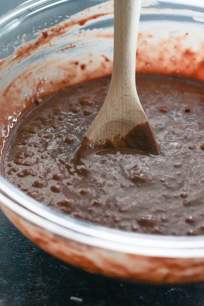 Cake batter being mixed in a glass bowl with a wooden spoon.