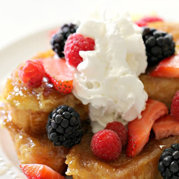 A plate of French toast topped with mixed berries, including raspberries, blackberries, and strawberry slices, finished with a dollop of whipped cream.