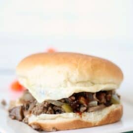 A sandwich with a white bun, filled with ground beef, onions, and pickles, placed on a white surface.