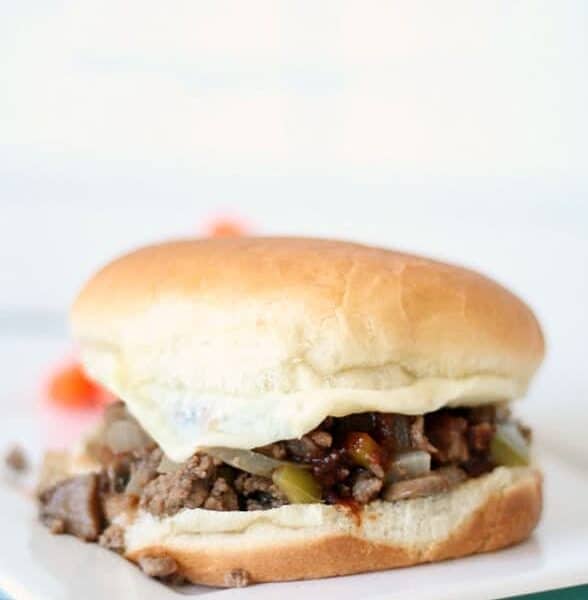 A sandwich with a white bun, filled with ground beef, onions, and pickles, placed on a white surface.