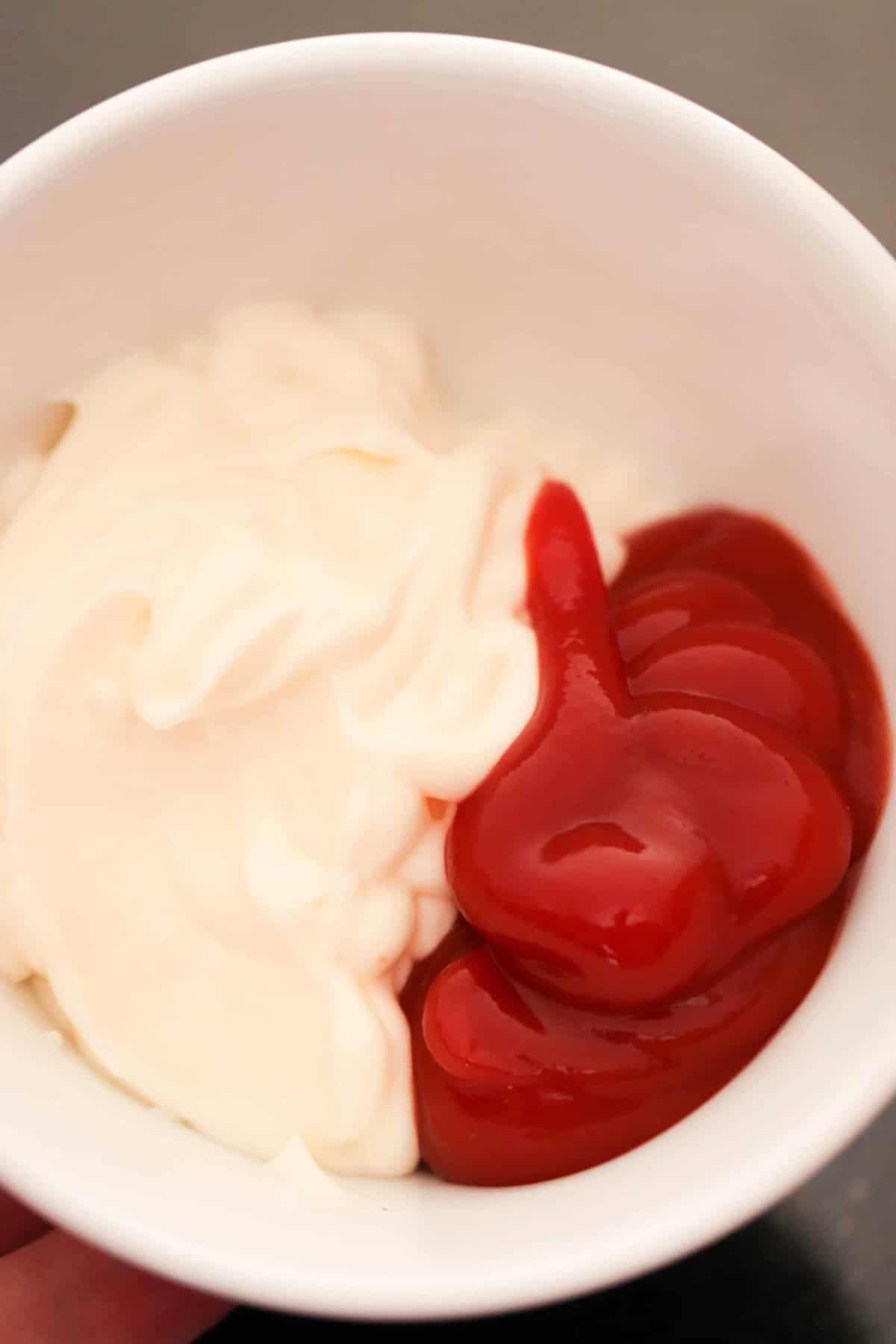 A white bowl containing mayonnaise and ketchup side by side on a dark surface.