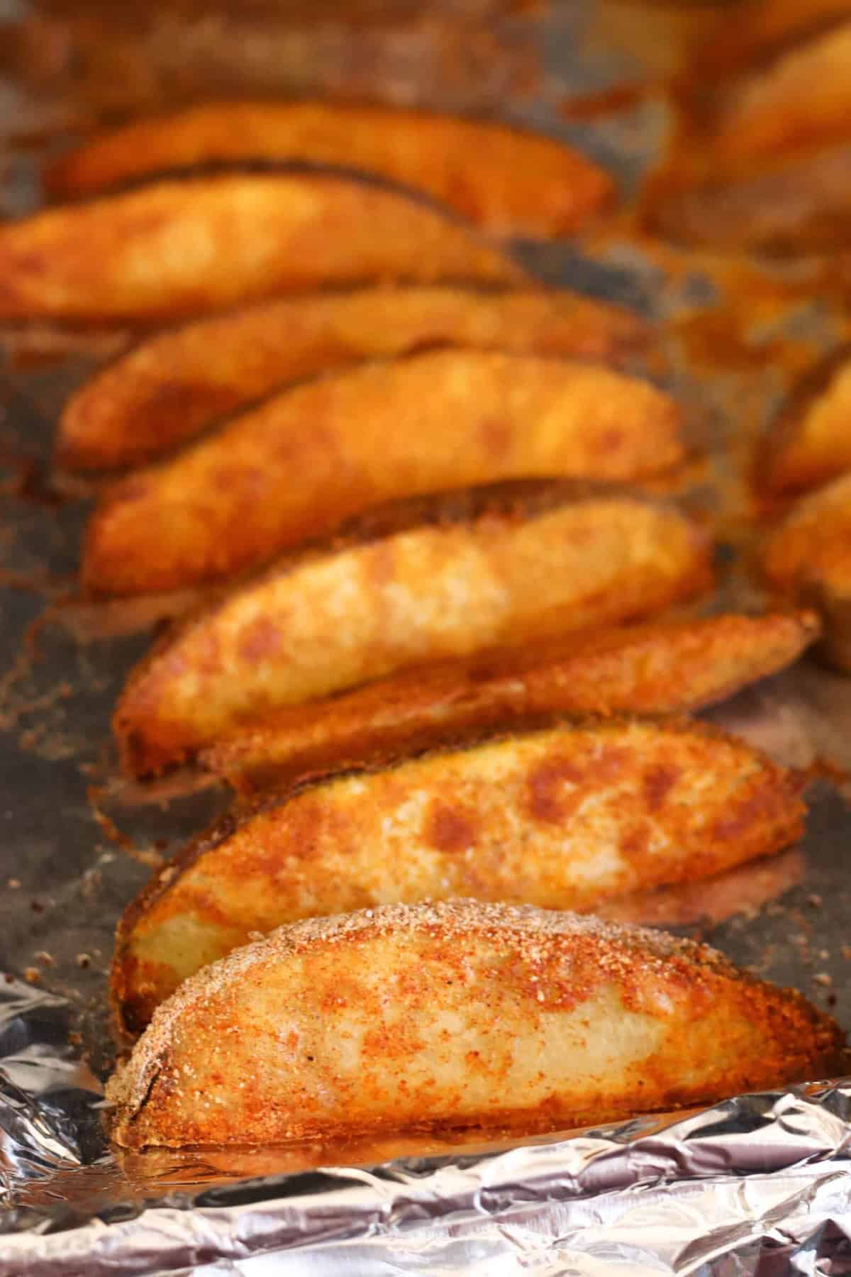 Baked potato wedges seasoned and arranged on a foil-lined baking sheet.