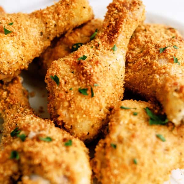 Close-up of several breaded and baked chicken drumsticks garnished with chopped parsley on a white plate.