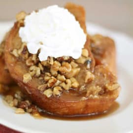 Two slices of caramel French toast topped with whipped cream and chopped nuts on a white plate.