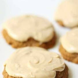 Close-up of four cookies topped with light-colored glaze, placed on a white surface. The cookies have a rough texture and an irregular, rounded shape.