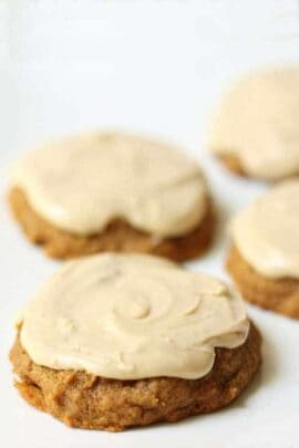 Close-up of four cookies topped with light-colored glaze, placed on a white surface. The cookies have a rough texture and an irregular, rounded shape.