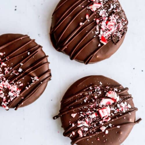 Three chocolate-covered round cookies topped with crushed peppermint candy and drizzled with additional chocolate.