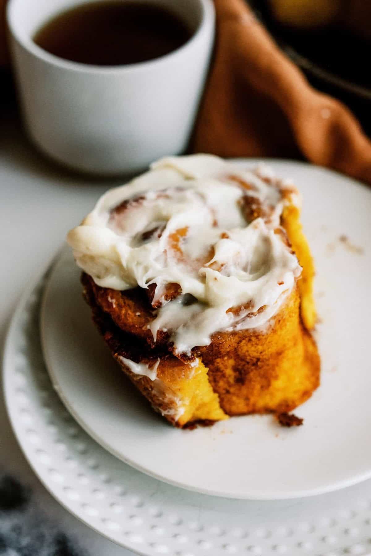 A cinnamon roll topped with white icing on a white plate.