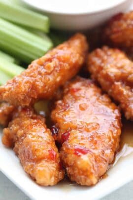 Close-up of glazed chicken tenders with celery sticks on a white plate.