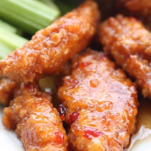 Close-up of glazed chicken tenders with celery sticks on a white plate.