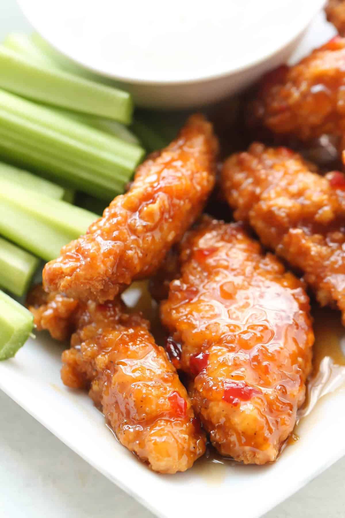 Close-up of glazed chicken tenders with sliced celery on a plate. A small bowl of dipping sauce is in the background.