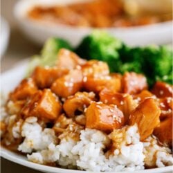 A plate of Slow Cooker Honey Sesame Chicken served over rice with sesame seeds on top and broccoli on the side.