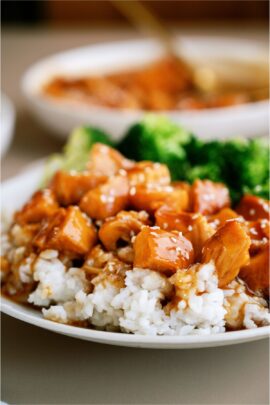 A plate of Slow Cooker Honey Sesame Chicken served over rice with sesame seeds on top and broccoli on the side.