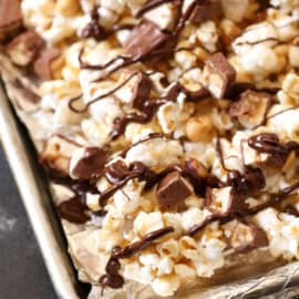 A close-up of a tray of popcorn mixed with chunks of chocolate and drizzled with melted chocolate.