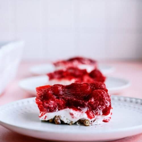 Close-up of a dessert plate featuring a square slice of layered strawberry pretzel salad with a pretzel crust, cream cheese center, and strawberry gelatin topping.