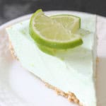 Slice of Key Lime Pie on a white plate topped with 2 slices of fresh lime.