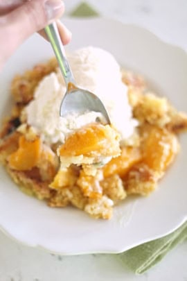 A slice of Peach Cobbler dump cake on a plate topped with ice cream