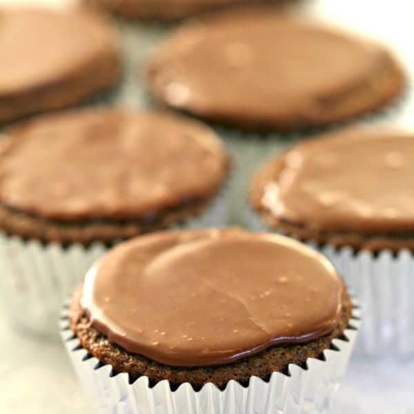 Chocolate cupcakes in silver wrappers with smooth, shiny frosting arranged in a group.