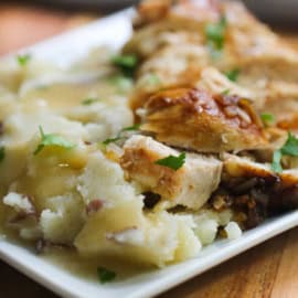 A plate of mashed potatoes topped with gravy and slices of roasted meat, garnished with chopped herbs.