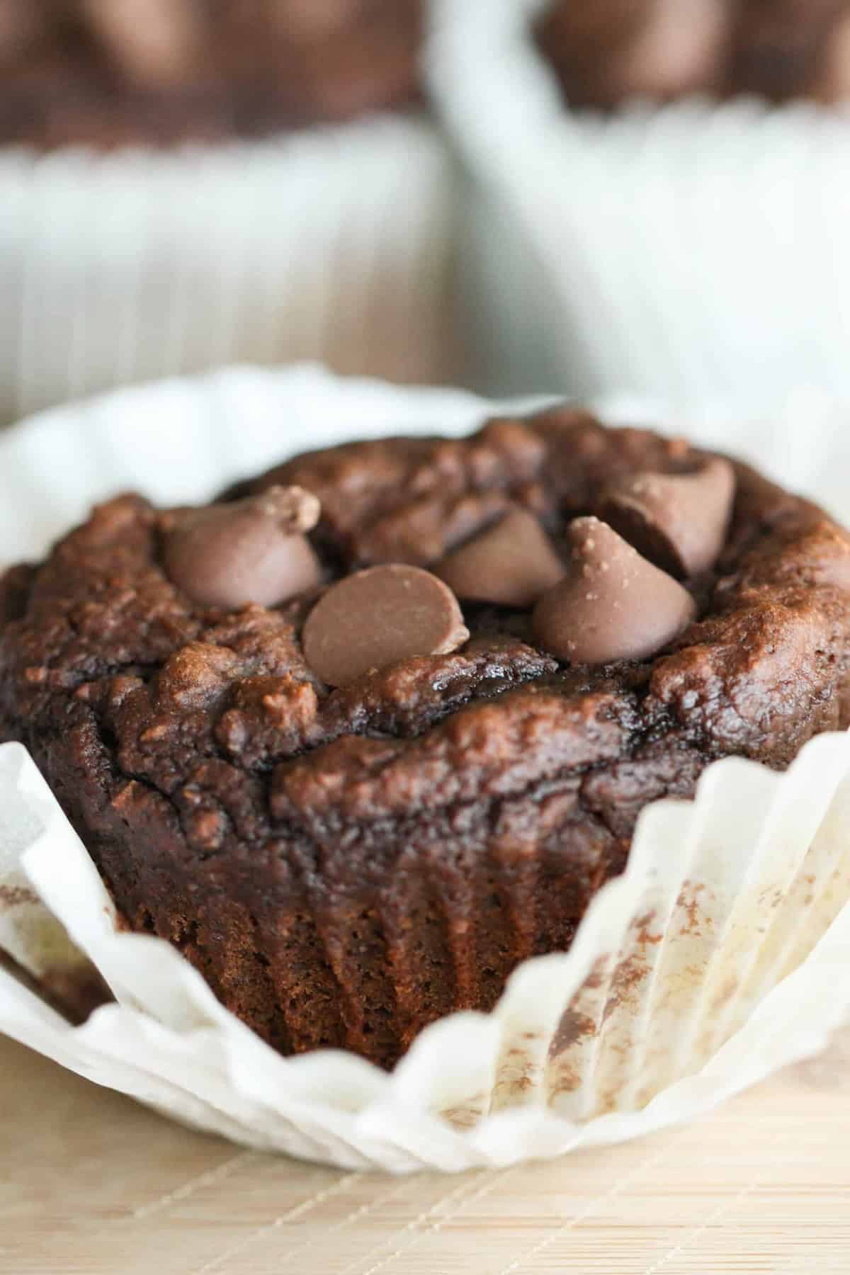 Close-up of a pumpkin chocolate muffin with chocolate chips on top, placed in a white paper liner.