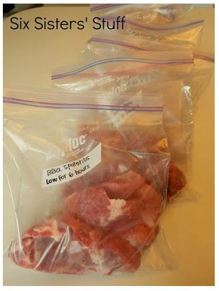 Four plastic bags filled with marinated meat, labeled \"BBQ Spareribs Low for 6 hours,\" arranged in a row on a counter.