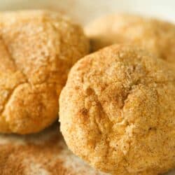 Three cinnamon dusted cookies on a white surface with additional cinnamon sprinkled around.