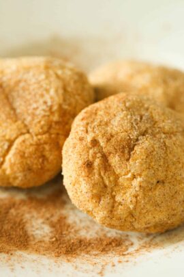 Three cinnamon dusted cookies on a white surface with additional cinnamon sprinkled around.