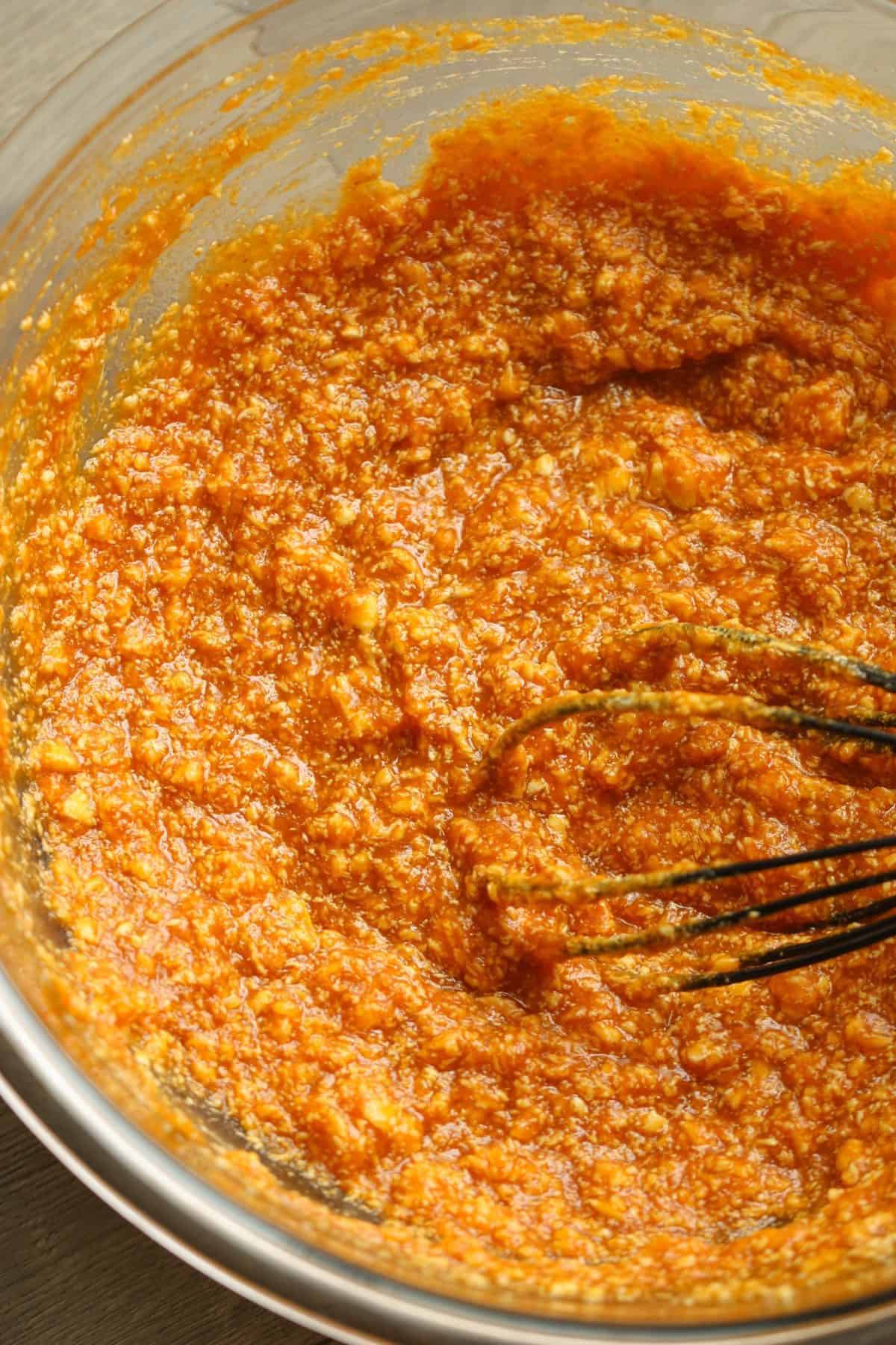 A whisk stirring a bowl of orange and brown textured mixture.