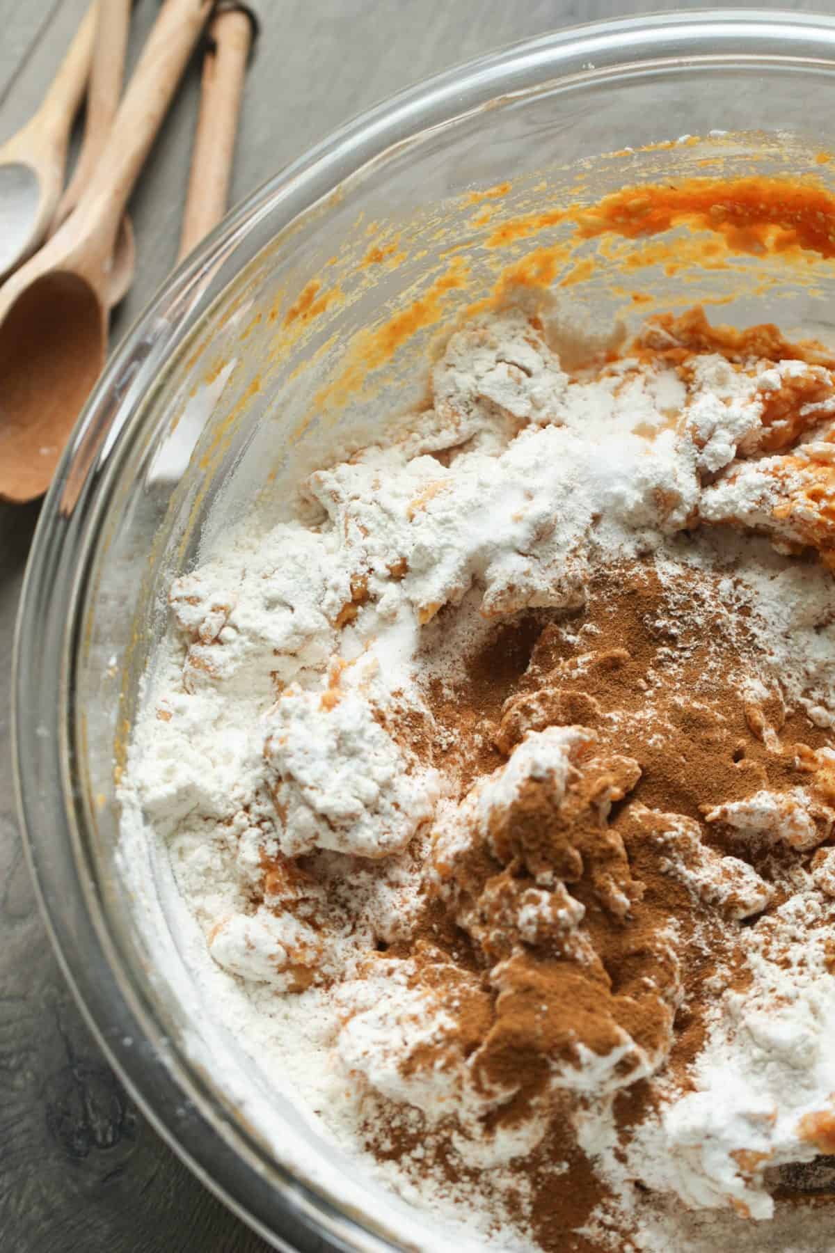 A mixing bowl with flour, cinnamon, and wet ingredients partially mixed. Three wooden spoons are laid beside the bowl.