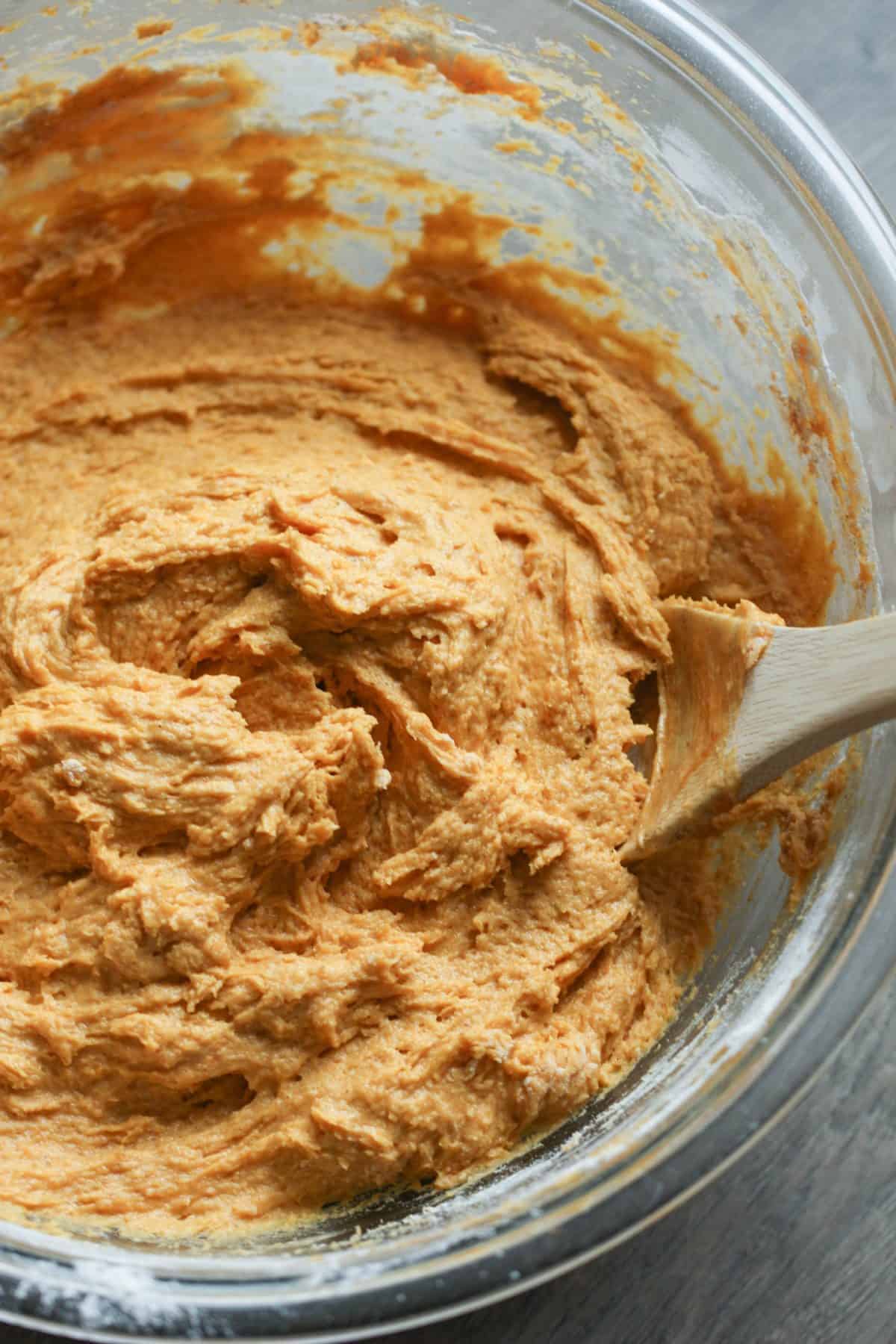 A mixing bowl contains a thick, light brown batter with a wooden spoon partially submerged in it.