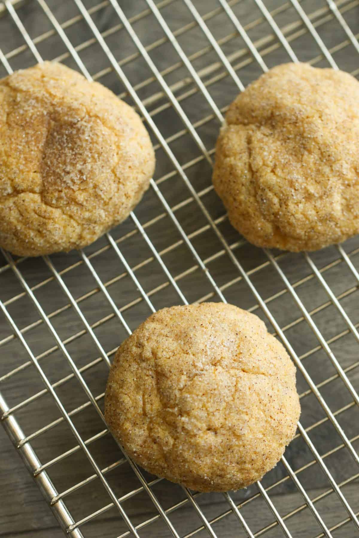 Three cinnamon sugar-coated cookies are cooling on a metal wire rack.