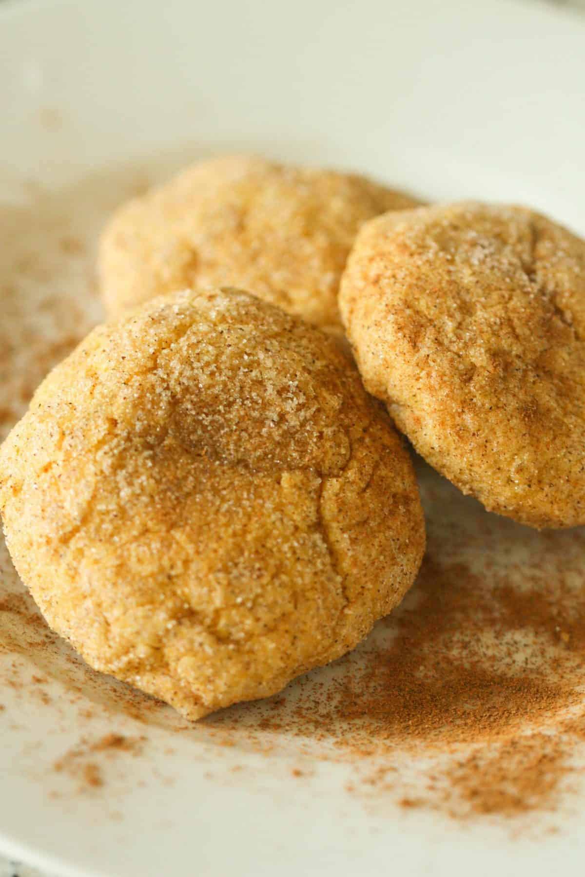 Three sugar-coated snickerdoodle cookies are arranged on a white plate dusted with cinnamon.