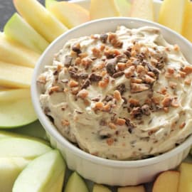 Sliced green apples in a circle surrounding a bowl of cream cheese toffee dip.