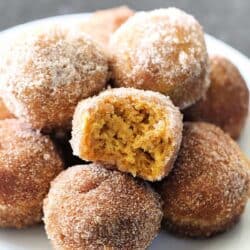 A plate of sugar-coated pumpkin donut holes, with one donut hole broken in half to show the inside texture.