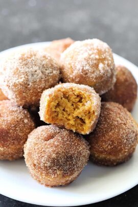 A plate of sugar-coated pumpkin donut holes, with one donut hole broken in half to show the inside texture.