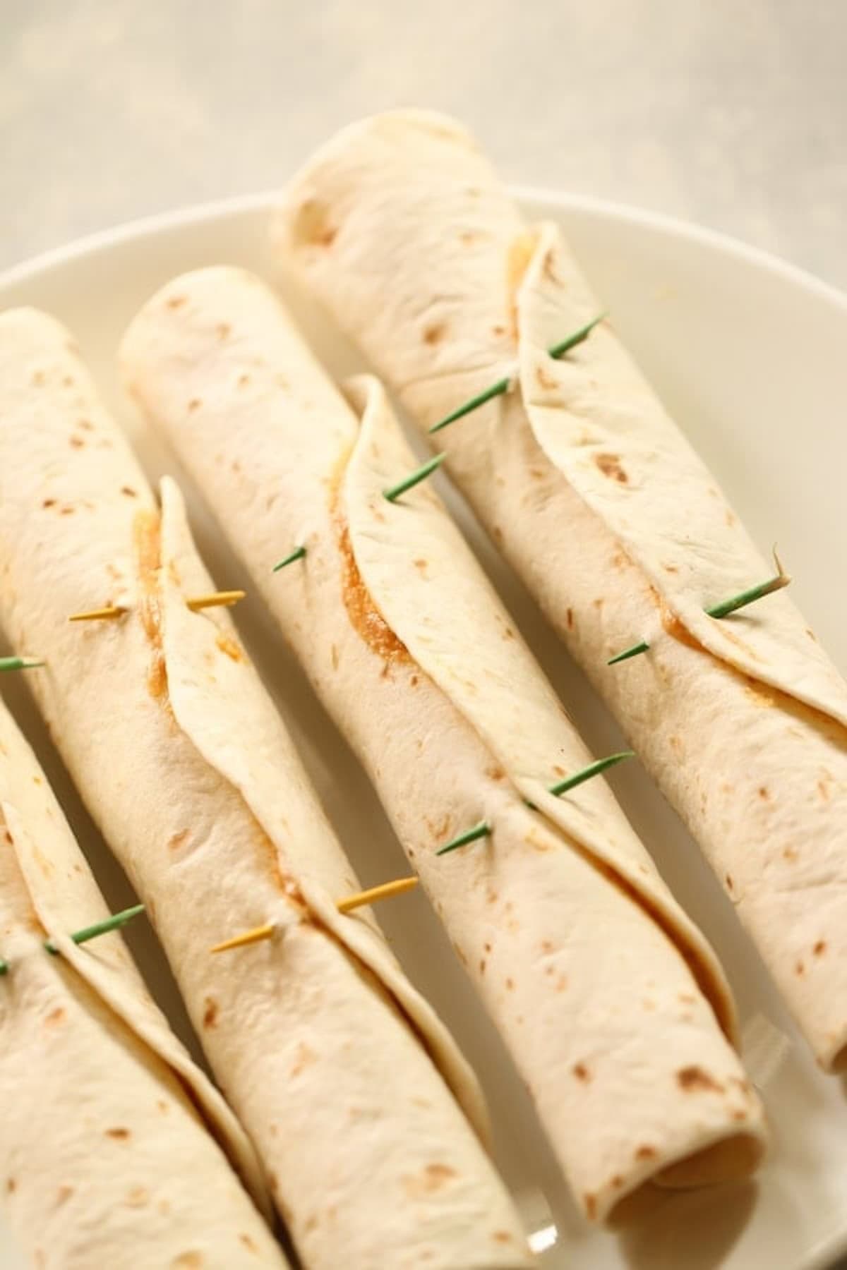 Four rolled tortillas secured with toothpicks are arranged on a white plate.