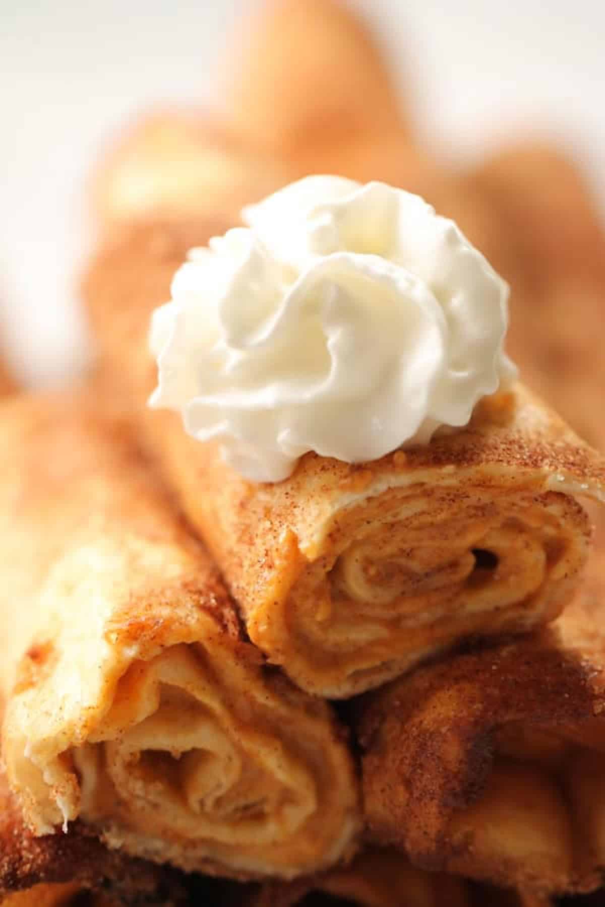 Close-up of rolled tortillas sprinkled with cinnamon and sugar, topped with a dollop of whipped cream.