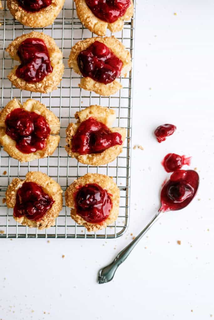 Cherry Cheesecake Cookies on a cooling rack with a spoon full of cherry pie filling.