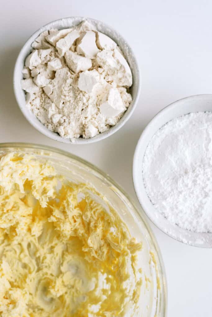 Wet cookie dough in a mixing bowl with powdered sugar and flour in separate small bowls.