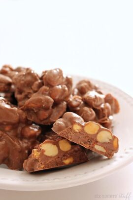 A plate with clusters of chocolate-covered nuts. Some pieces are cut to show the interior.