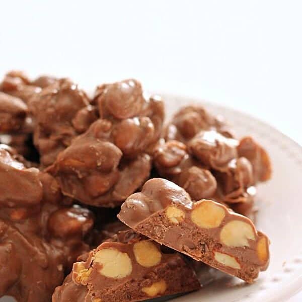 A plate with clusters of chocolate-covered nuts. Some pieces are cut to show the interior.