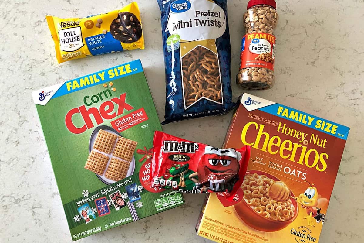 A variety of snacks on a countertop, including Corn Chex, Honey Nut Cheerios, pretzels, peanuts, a Toll House cookie, and a pack of M&M's.