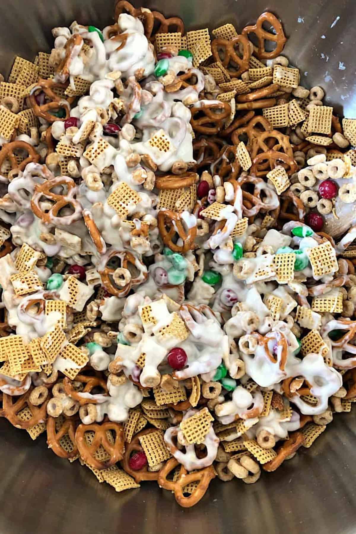 A snack mix with pretzels, cereal, nuts, and colored candies coated in white frosting.