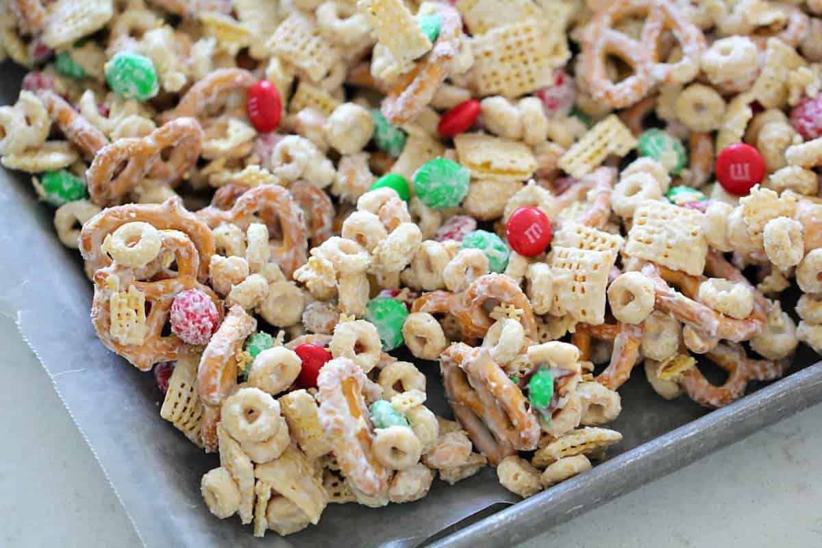 A bowl of snack mix containing pretzels, cereal squares, colorful candies, and round cereal pieces.