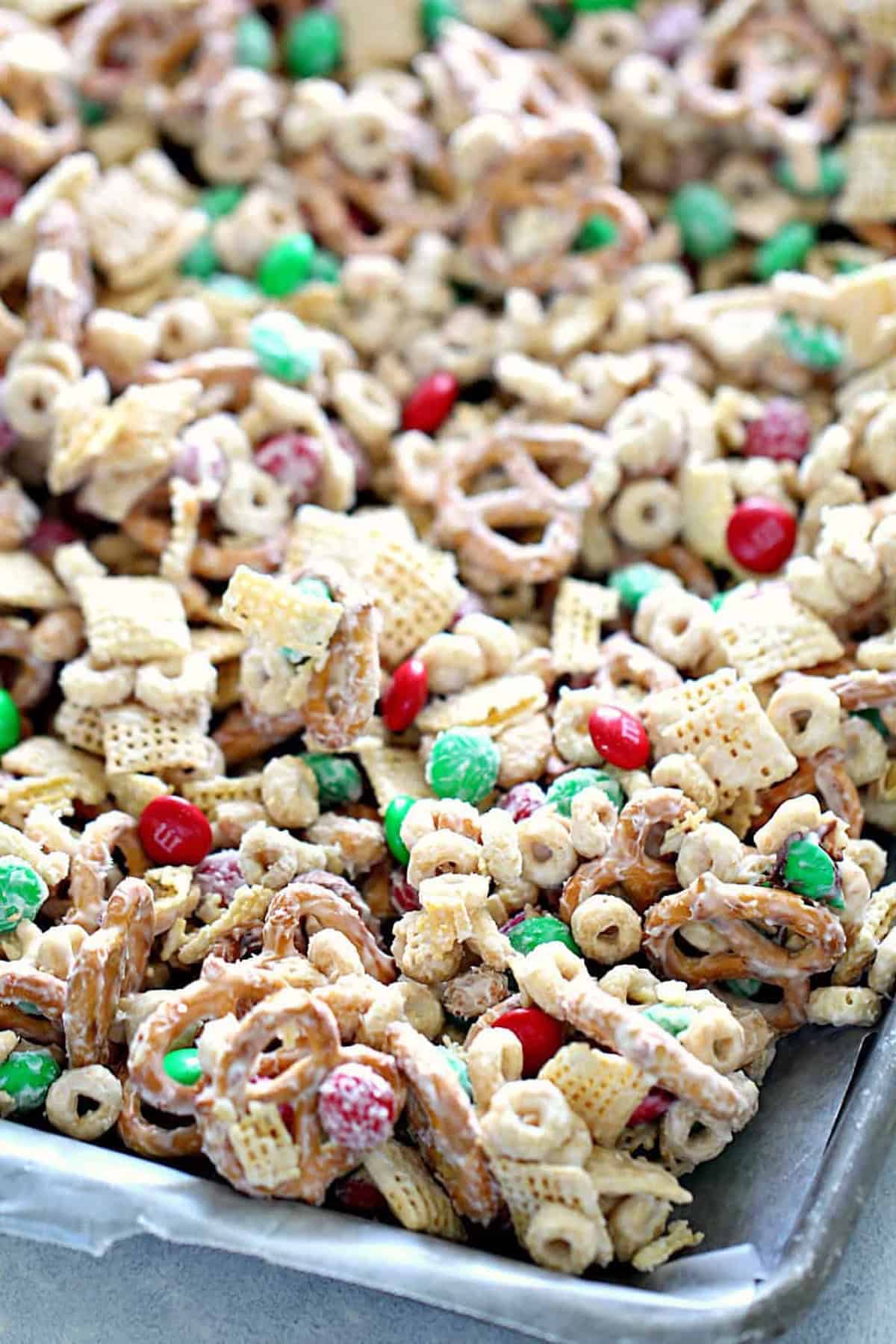 A tray filled with a mix of pretzels, cereal, candy-coated chocolates, and popcorn, all coated with a white substance.