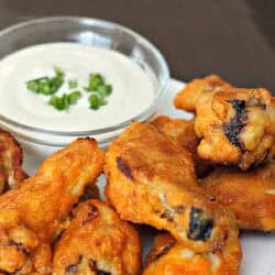 Buffalo chicken wings on a white plate with a side of creamy dipping sauce garnished with chopped herbs.